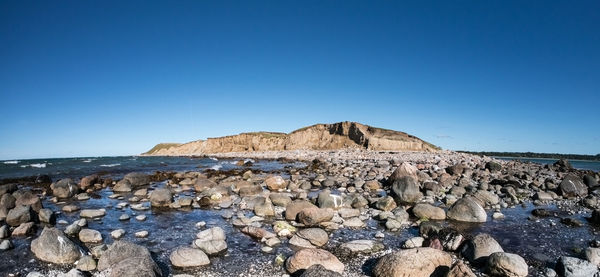 Rocks on beach against clear blue sky