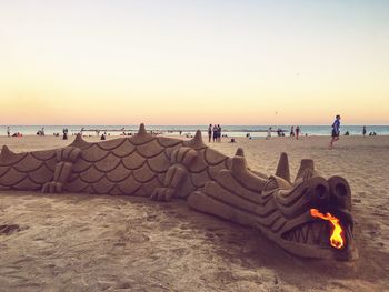 Sand sculpture by crowd at beach during sunset