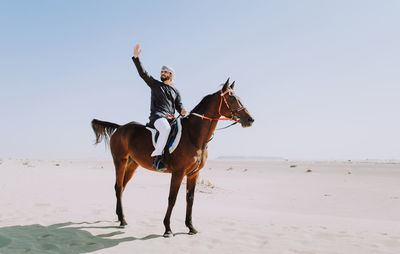 Young man taking selfie with mobile phone riding horse at desert