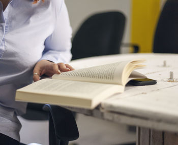 Midsection of woman reading book on table