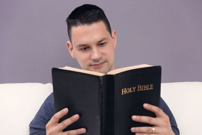 Portrait of young man reading book against gray background