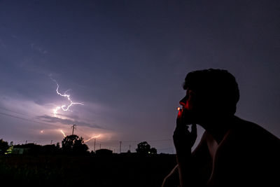 Man smoking cigarette against sky at night