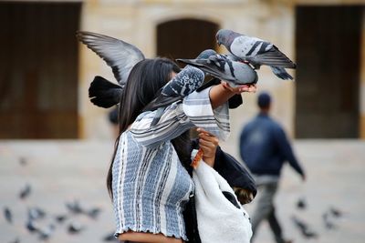 Low angle view of young woman standing on street with many pigeon / dove