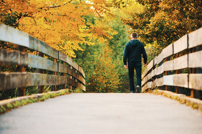 Rear view of man walking on footpath during autumn