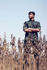 Low angle view of young man with arms crossed standing on field against clear sky