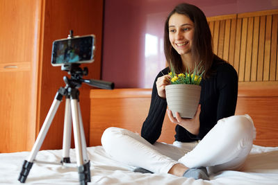 Portrait of smiling woman holding camera at home