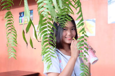 Portrait of smiling young woman drinking juice by plants