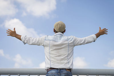 Rear view of man standing with arms outstretched against sky