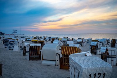 Hooded chairs on beach against sky during sunset