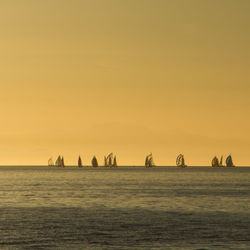 Boats at sea against clear sky during sunset