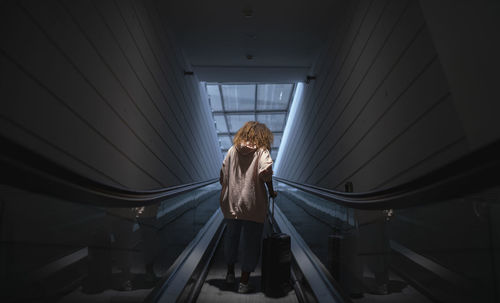 Young woman holding suitcase standing on escalator at airport