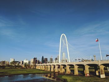 Bridge over river by buildings against blue sky