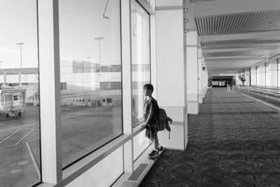 Side view of boy with backpack looking through window while standing at airport