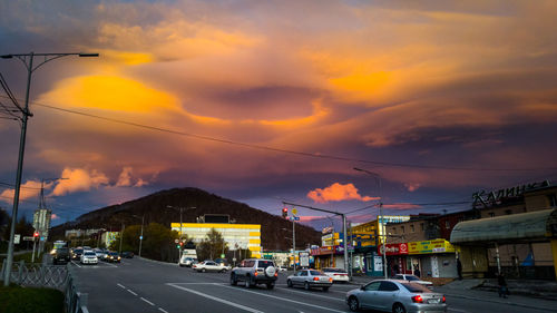 Cars on street against sky at sunset