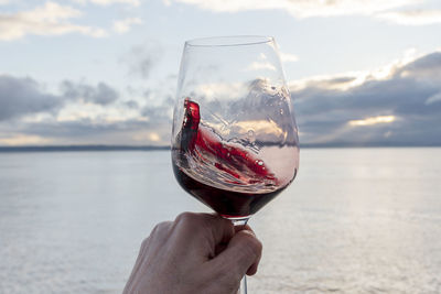 Swirling red wine point of view over sea with dramatic sunset sky.