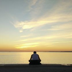 Silhouette man sitting on beach against sky during sunset