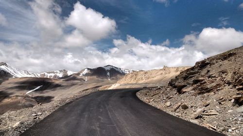 Empty road leading towards mountains against cloudy sky