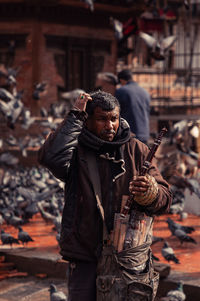 Young man holding wind instruments while standing on road in city