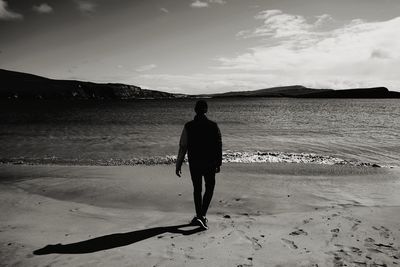 Full length rear view of man walking on beach against sky