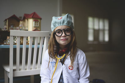 Portrait of cute girl in doctor's costume sitting at home