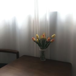 Flower vase on table against window at home