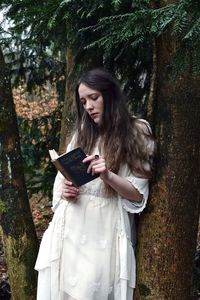 Young woman holding while standing by tree