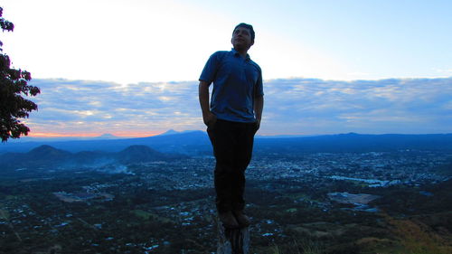 Man standing on rock against landscape during sunset