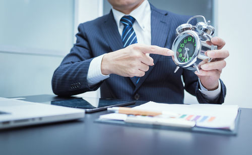 Midsection of businessman holding alarm clock at desk in office