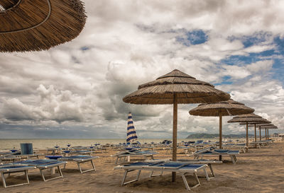 Lounge chairs and parasols at beach against cloudy sky