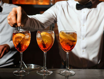Three glass glasses with an aperol spritz cocktail are on bar bartender is stirring one of aperitifs