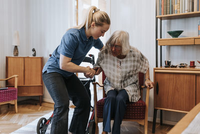 Female caregiver supporting senior woman while sitting on chair at home