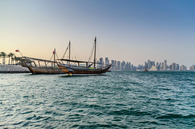 Sailboats in sea by buildings against clear sky