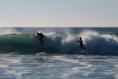 Men surfing in sea against clear sky