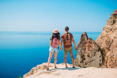 Rear view of women standing on rock by sea against clear sky