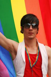 Young man wearing sunglasses standing against multi colored umbrella