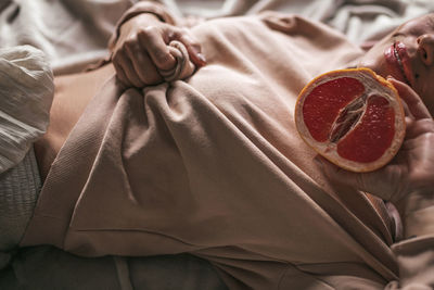 Midsection of woman with grapefruit lying on bed at home