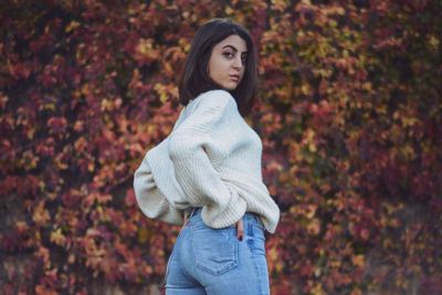 Side view of young woman standing against autumn leaves