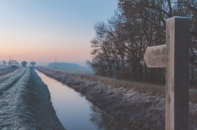 Road by canal against sky during sunset