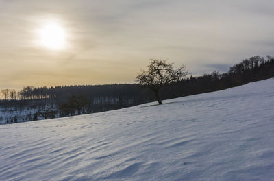 Snow covered landscape against sky during sunset