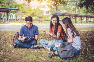 Friends studying while sitting on grassy field at park