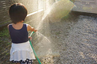 Rear view of girl spraying water at back yard