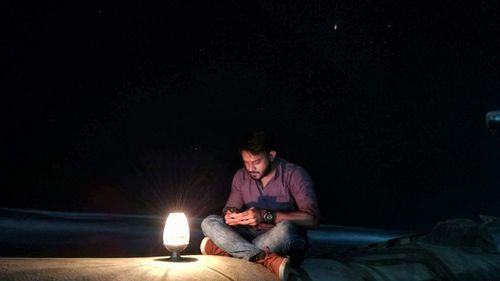 Full length of man sitting by illuminated lamp on footpath