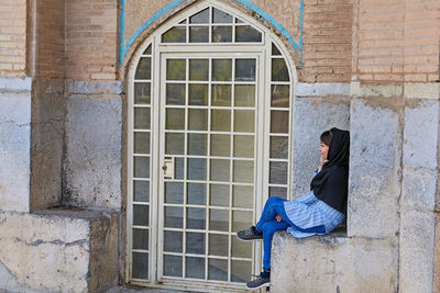 Side view of woman sitting outside building