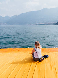 Rear view of woman sitting on beach against sky