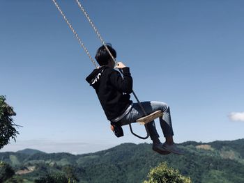 Low angel view of woman sitting on swing against sky