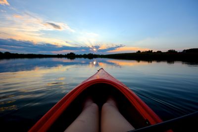 Midsection of woman on kayak in lake against sky during sunset