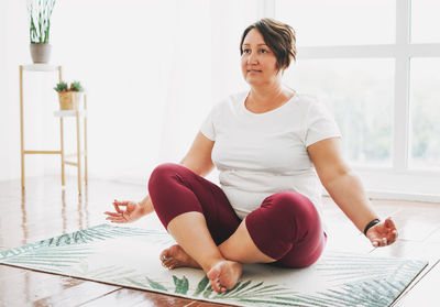 Adult charming brunette woman plus size body positive practice yoga at bright studio