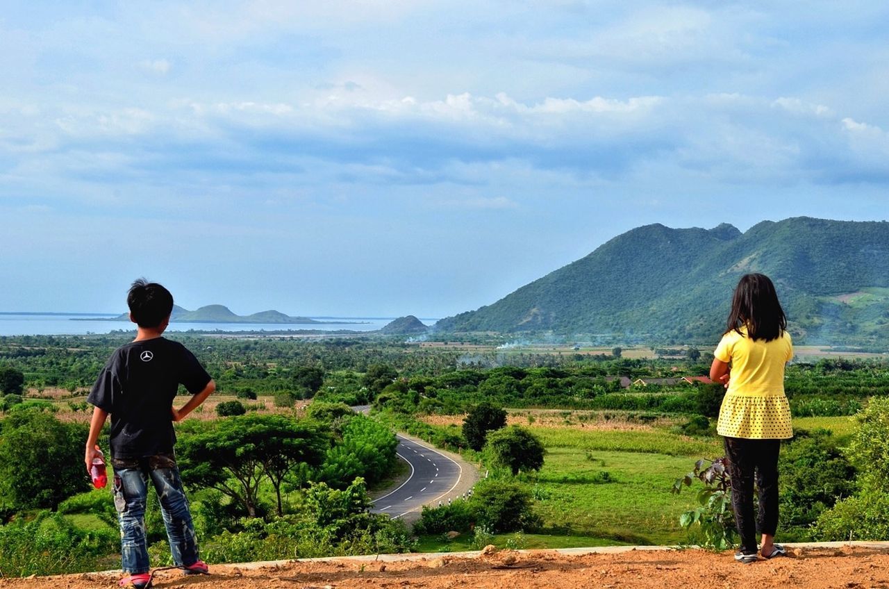 mountain, lifestyles, sky, casual clothing, landscape, full length, rear view, leisure activity, mountain range, tranquil scene, scenics, tranquility, beauty in nature, nature, cloud - sky, men, grass, standing