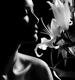 Close-up of woman smelling flowers against black background