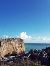 Rocks by sea against blue sky